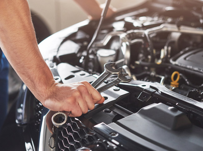 Mechanic holding wrenches over a vehicle engine, emphasizing collision repair services at Lake Area Collision, Inc.
