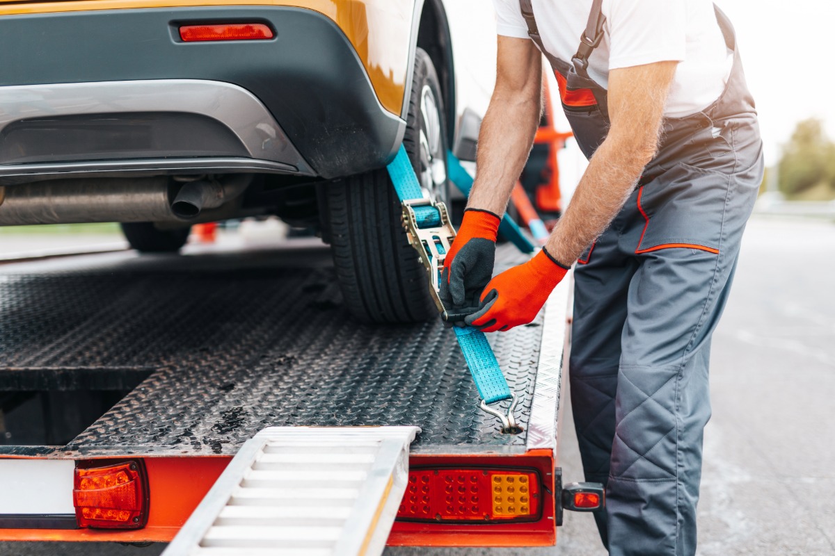 Towing professional securing vehicle with blue straps on tow truck, emphasizing reliable roadside assistance and vehicle transport services.