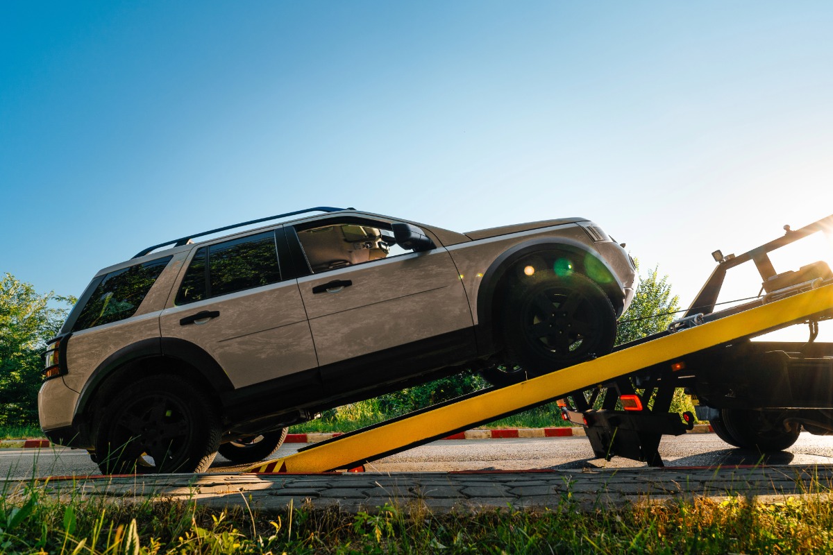 Vehicle being towed onto a flatbed truck, showcasing reliable roadside assistance and towing services by Lake Area Collision, with a clear blue sky in the background.