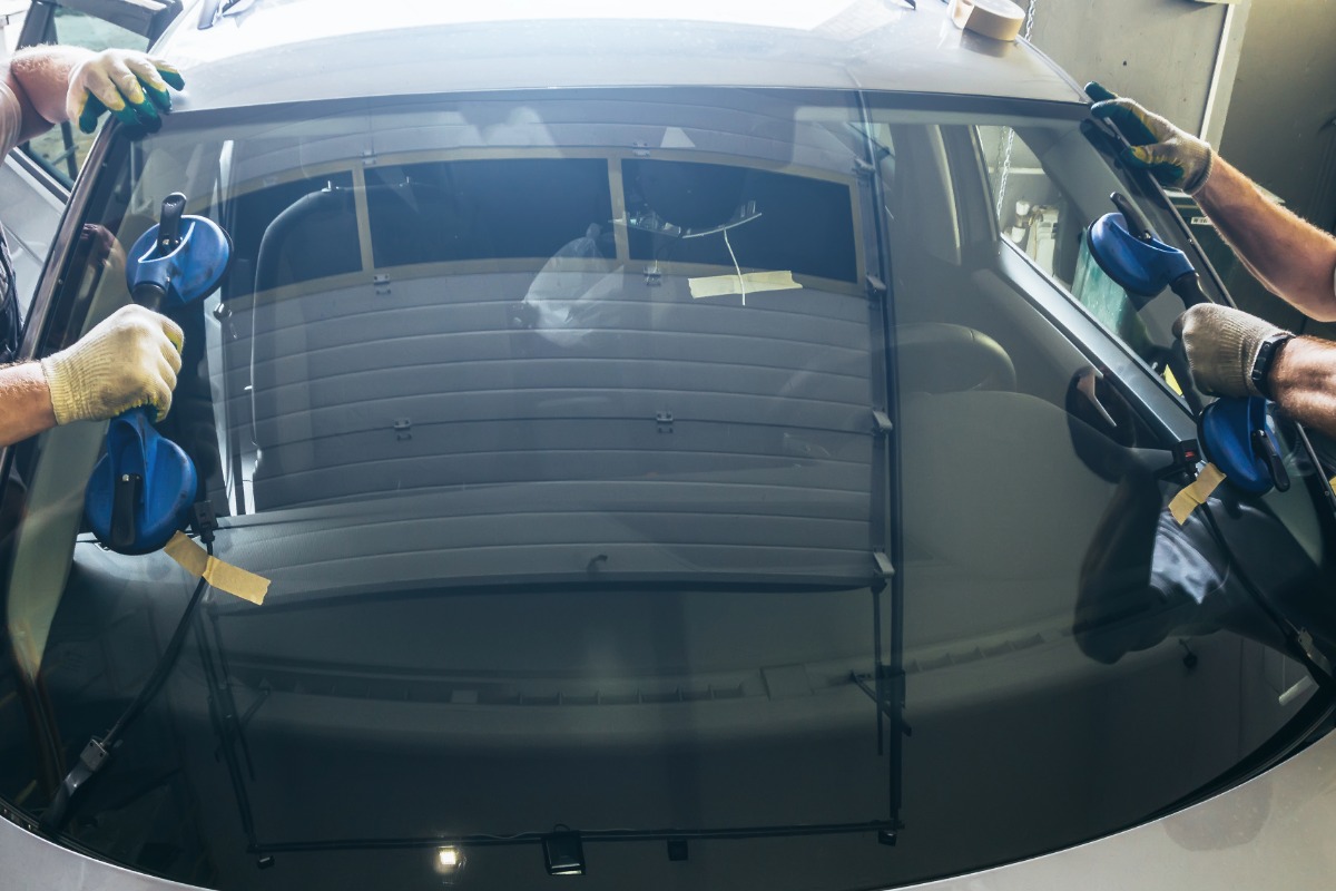 Technicians performing auto glass replacement on a vehicle's windscreen, showcasing suction cups and tools in a repair shop setting.